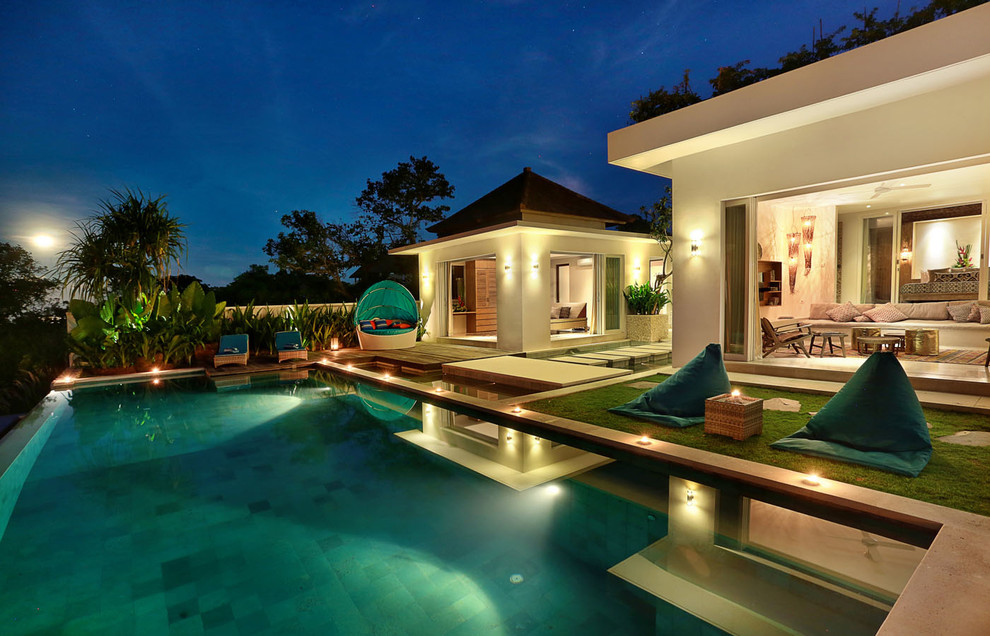 Foto på en stor tropisk infinitypool på baksidan av huset, med poolhus och naturstensplattor