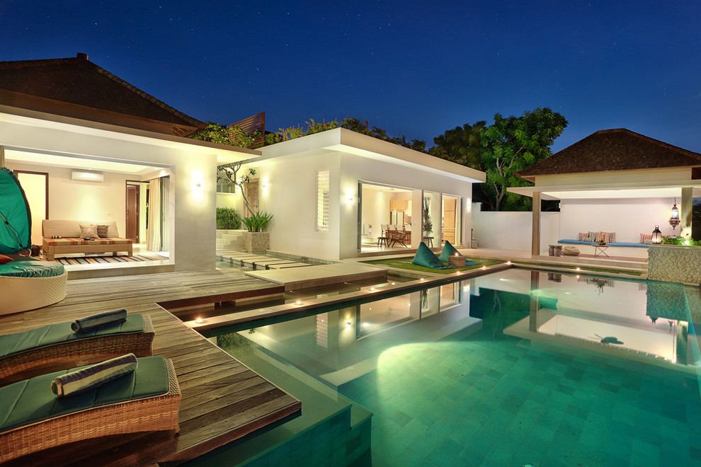 Immagine di una grande piscina a sfioro infinito tropicale rettangolare dietro casa con una dépendance a bordo piscina e pavimentazioni in pietra naturale