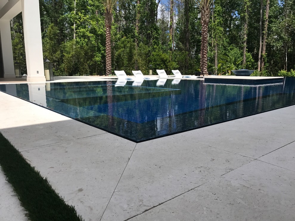 Ispirazione per un'ampia piscina a sfioro infinito minimalista personalizzata dietro casa con fontane