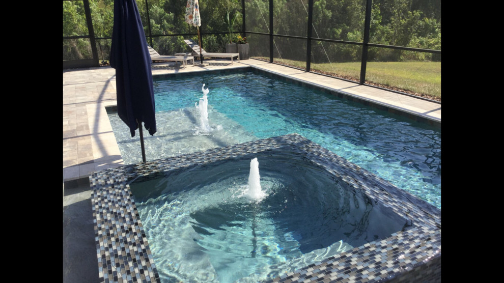 Immagine di una grande piscina naturale moderna personalizzata dietro casa con fontane e pavimentazioni in cemento