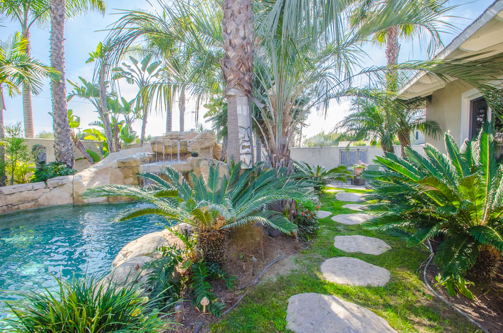 Foto på en stor tropisk baddamm på baksidan av huset, med vattenrutschkana och naturstensplattor