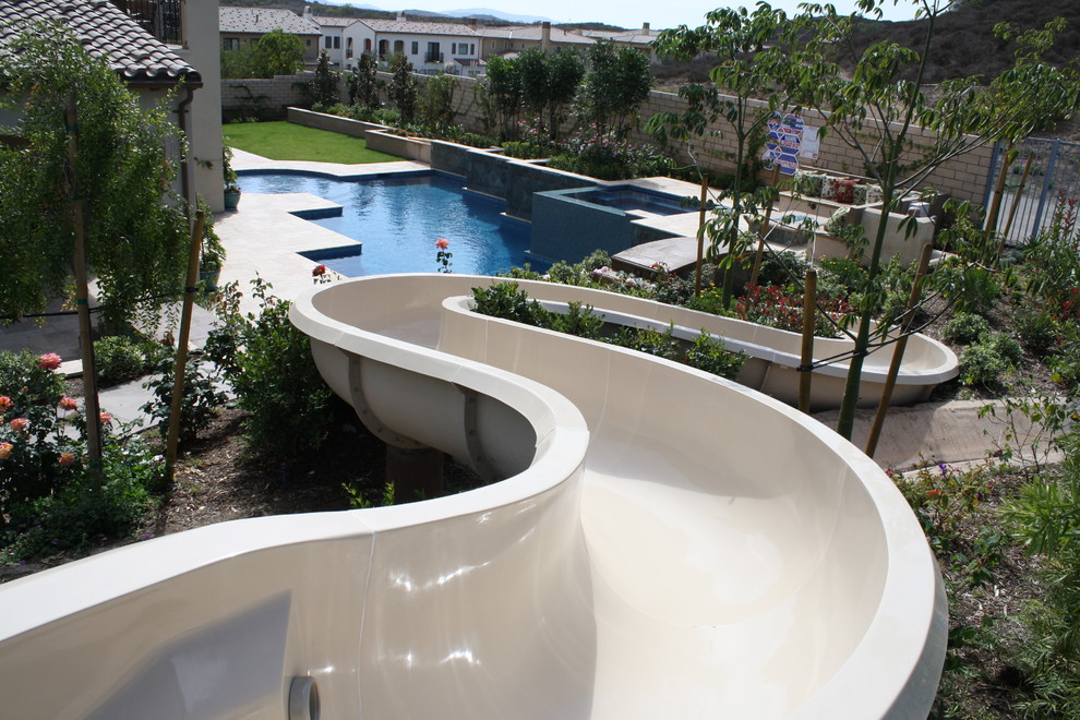 Geräumiges Mediterranes Sportbecken hinter dem Haus in rechteckiger Form mit Wasserrutsche und Natursteinplatten in Los Angeles