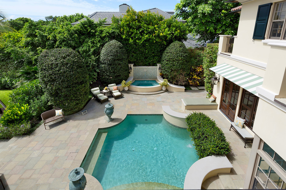 Photo of a medium sized mediterranean back custom shaped natural swimming pool in Miami with a water feature and stamped concrete.