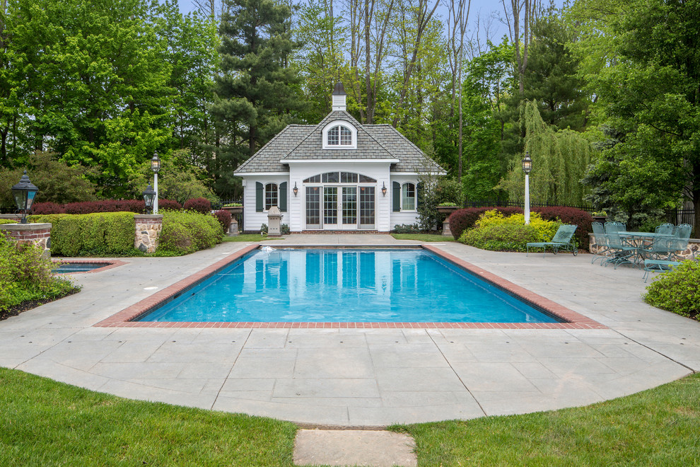 Modelo de casa de la piscina y piscina tradicional grande en patio trasero con suelo de hormigón estampado