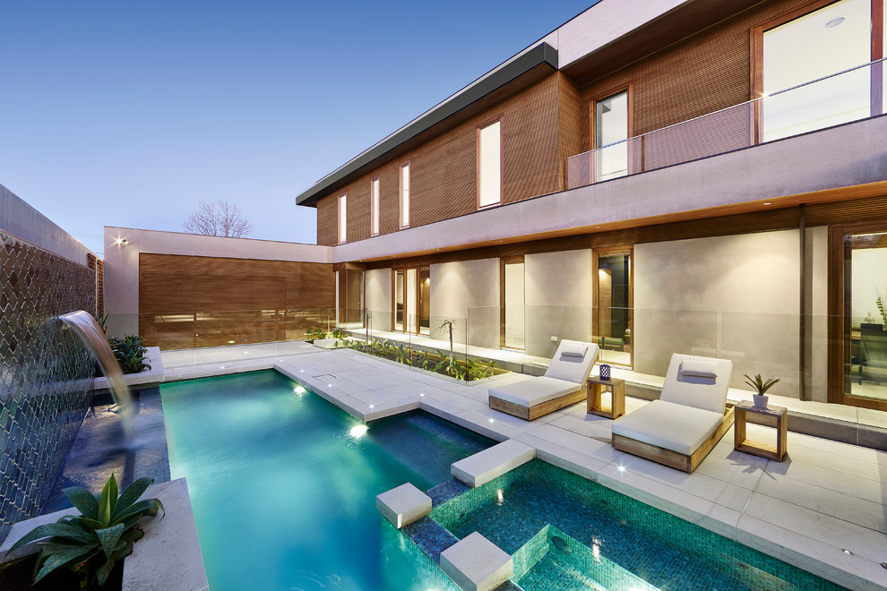 Diseño de piscina moderna a medida en patio trasero con adoquines de hormigón
