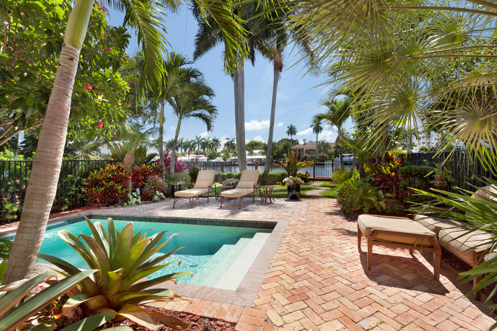 Imagen de piscina con fuente alargada exótica grande rectangular en patio trasero con adoquines de ladrillo