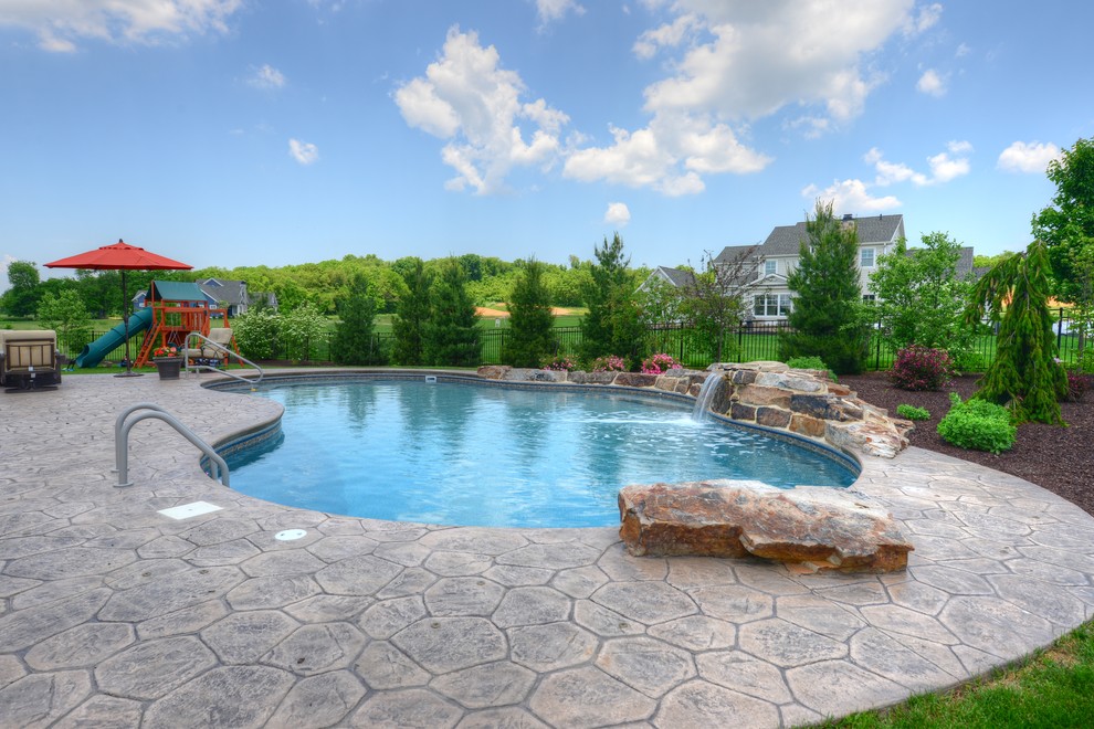 Imagen de piscina alargada clásica grande tipo riñón en patio trasero con adoquines de piedra natural