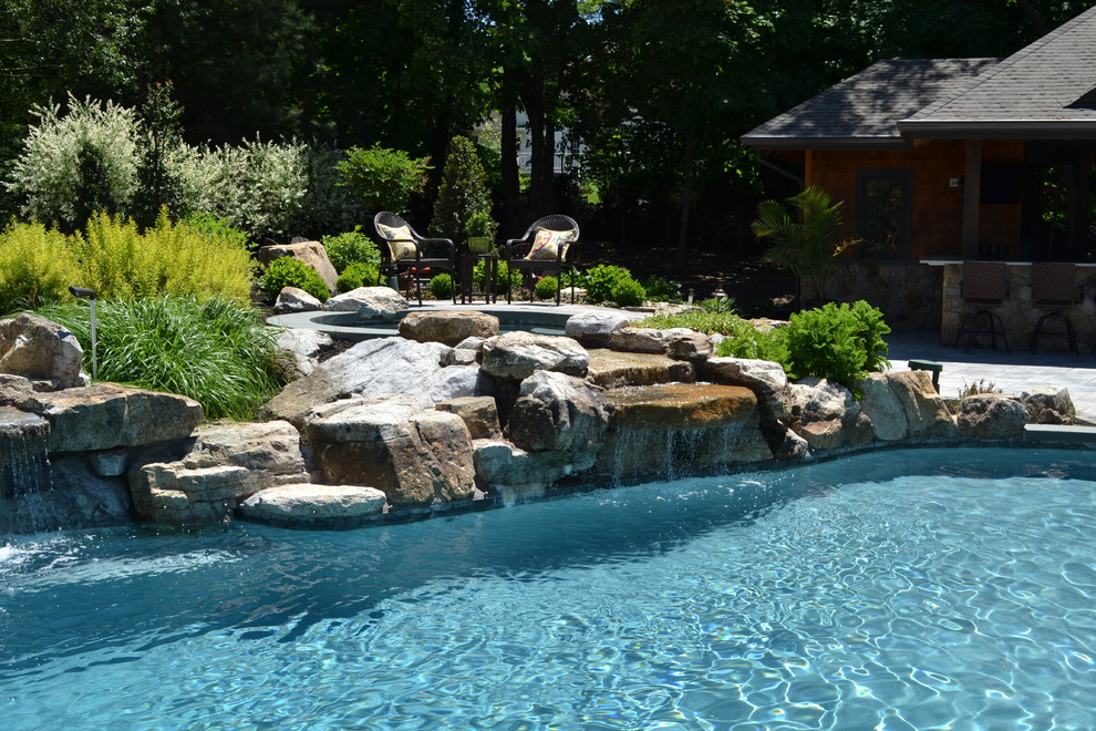 Imagen de piscina con fuente moderna grande a medida en patio trasero con adoquines de hormigón