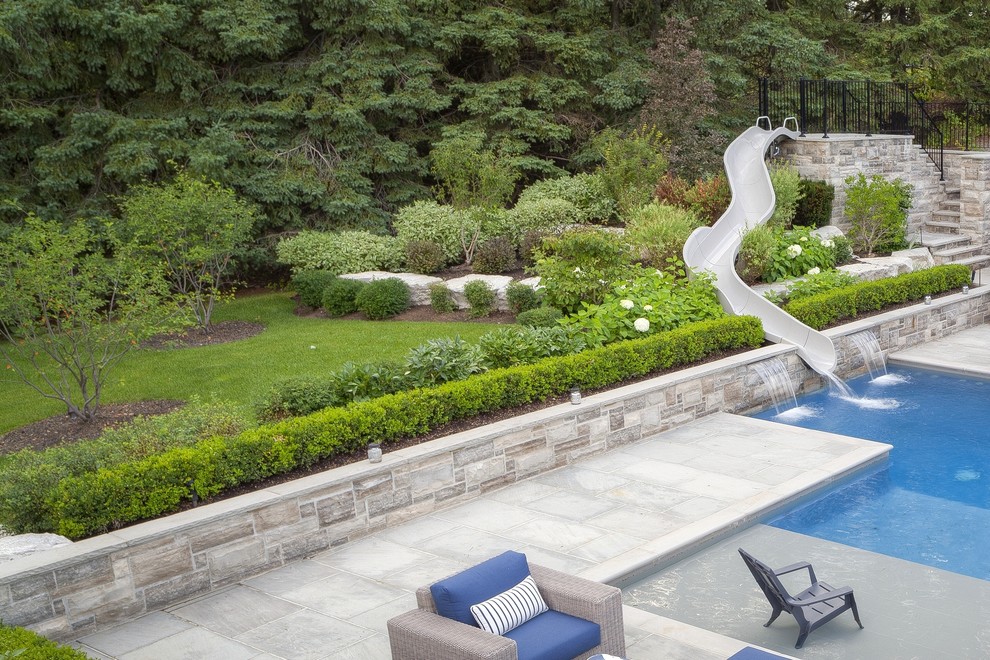 Ejemplo de piscina con tobogán alargada actual grande rectangular en patio lateral con adoquines de piedra natural