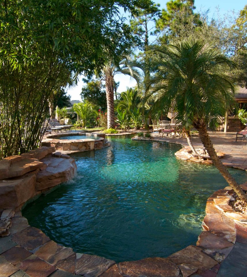 Aménagement d'une grande piscine arrière exotique sur mesure avec un bain bouillonnant et des pavés en pierre naturelle.