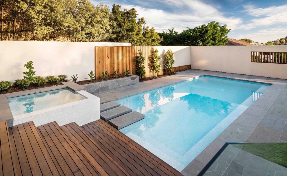Idée de décoration pour une grande piscine arrière et à débordement design rectangle avec un bain bouillonnant et des pavés en pierre naturelle.