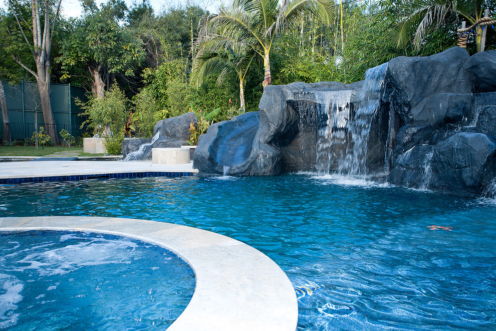 Стильный дизайн: естественный бассейн среднего размера, произвольной формы на заднем дворе в средиземноморском стиле с водной горкой и мощением тротуарной плиткой - последний тренд