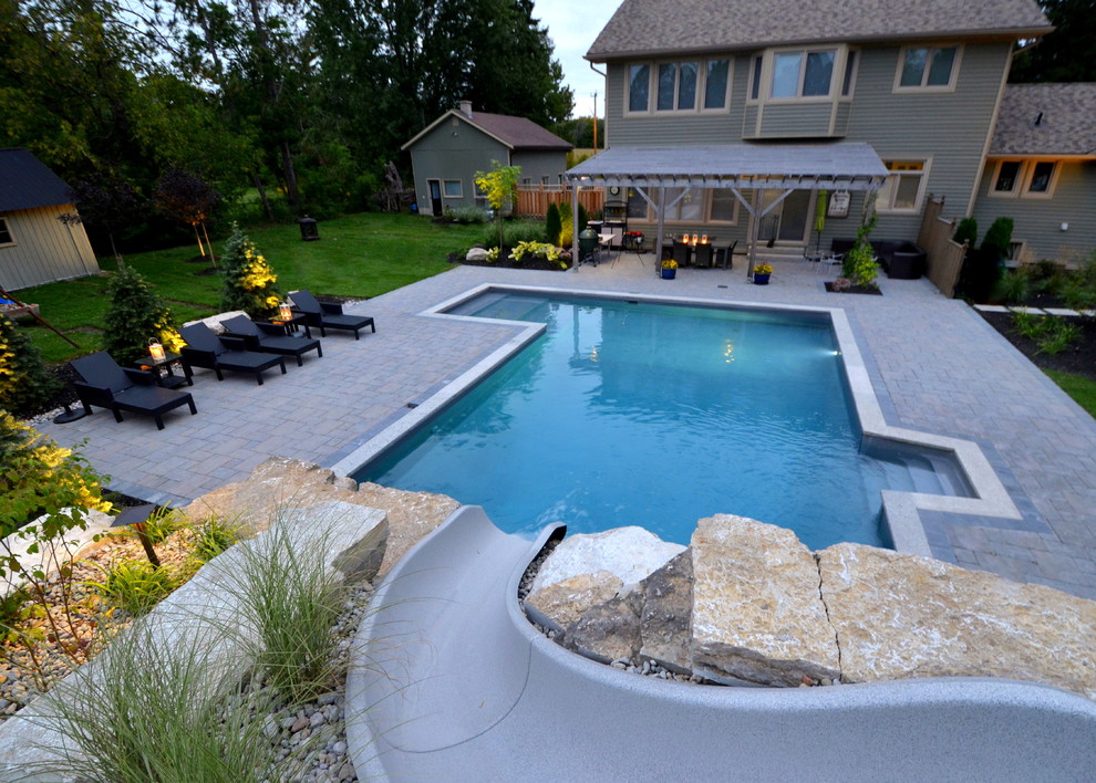 Modelo de piscina con tobogán contemporánea en forma de L en patio trasero con adoquines de hormigón