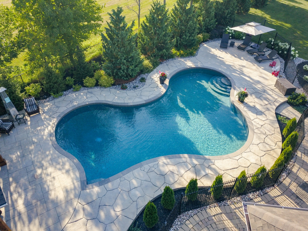 На фото: большой бассейн произвольной формы на заднем дворе в стиле неоклассика (современная классика) с покрытием из декоративного бетона