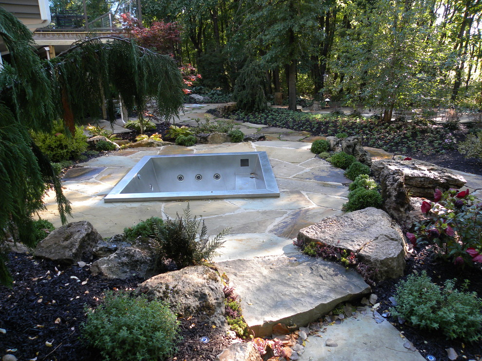 Cette photo montre une très grande piscine arrière chic sur mesure avec un bain bouillonnant et des pavés en pierre naturelle.