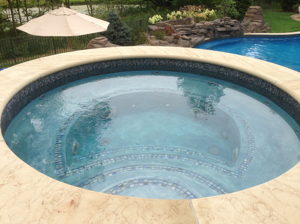 Idée de décoration pour une grande piscine arrière et naturelle chalet sur mesure avec un bain bouillonnant et des pavés en béton.