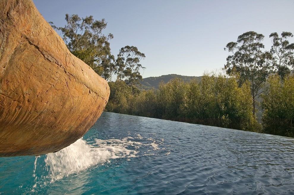 Cette photo montre une grande piscine à débordement et arrière exotique rectangle avec un toboggan et du béton estampé.