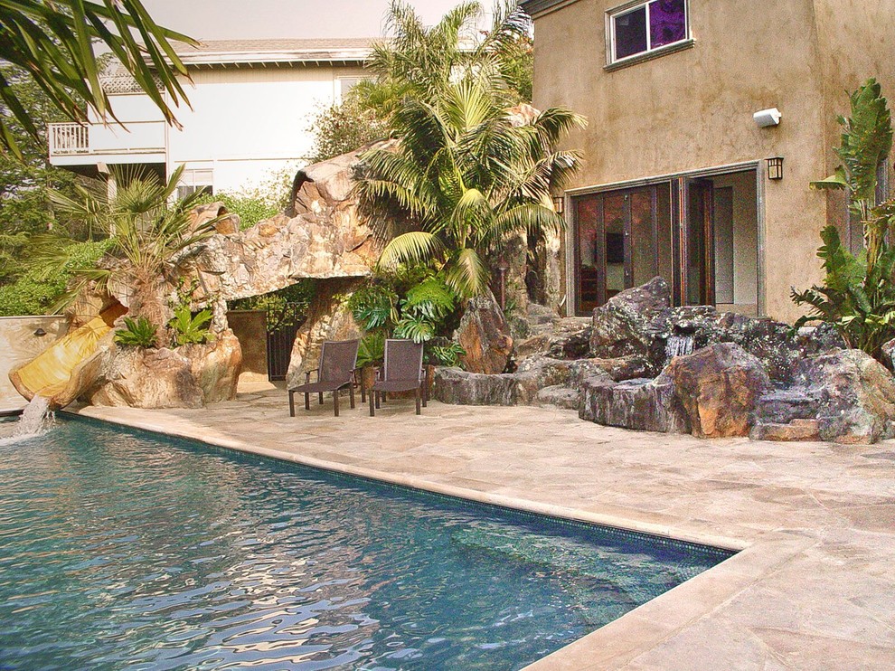 Foto di una grande piscina a sfioro infinito tropicale rettangolare dietro casa con un acquascivolo e cemento stampato
