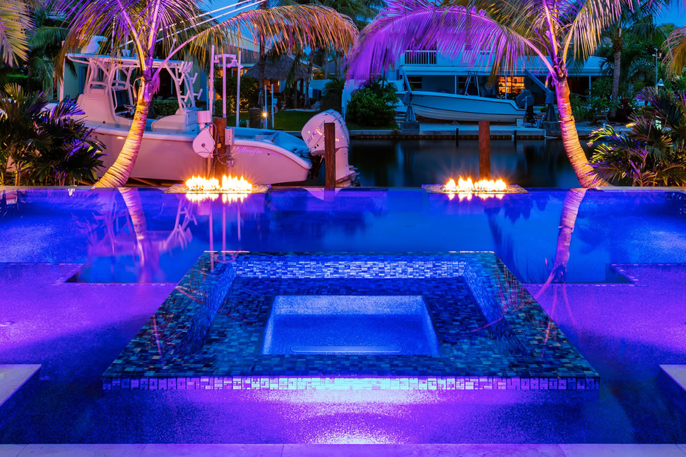 Esempio di una piscina a sfioro infinito tropicale personalizzata di medie dimensioni e dietro casa con una vasca idromassaggio e pavimentazioni in pietra naturale