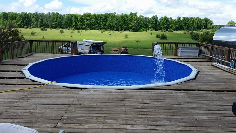 Modelo de piscina elevada grande redondeada en patio trasero con entablado