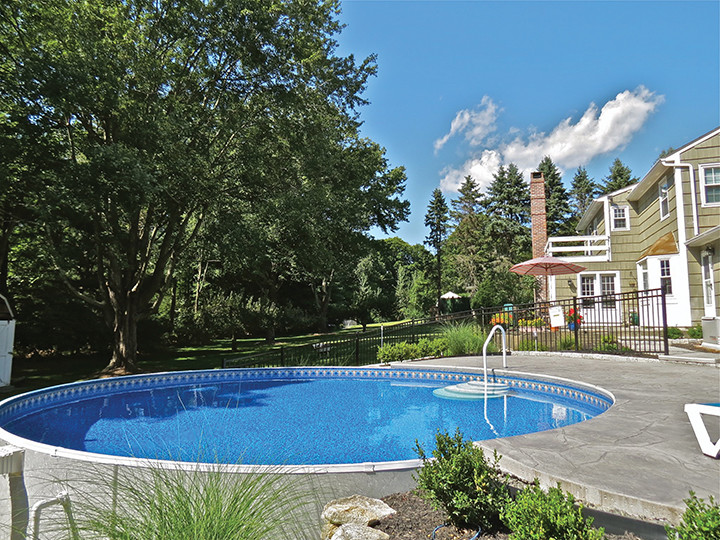 Foto de piscina elevada tradicional grande redondeada en patio trasero con suelo de hormigón estampado