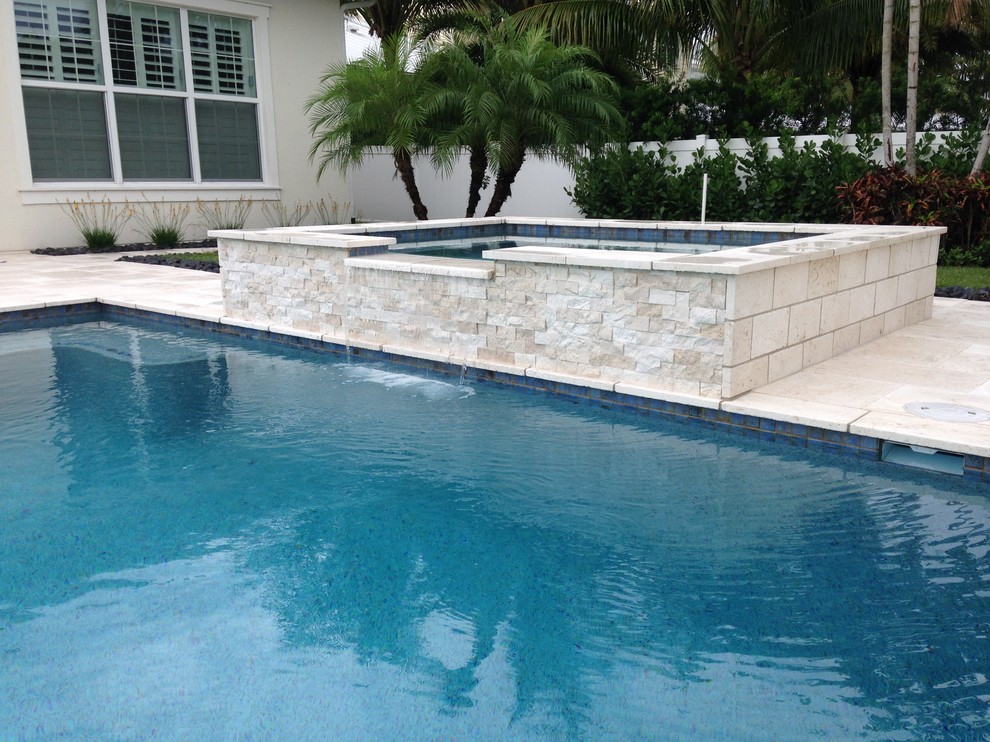 This is an example of a large contemporary back custom shaped natural swimming pool in Miami with a water feature.