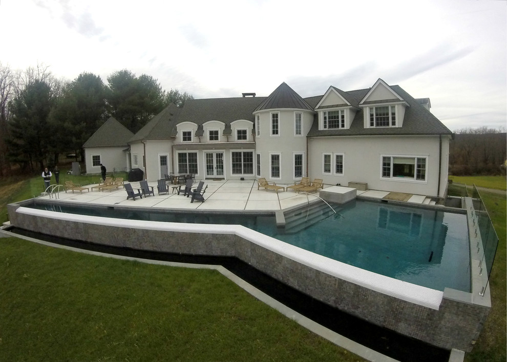 Imagen de piscina alargada de estilo de casa de campo grande en forma de L en patio trasero con losas de hormigón