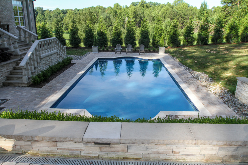 Foto de piscina alargada clásica grande rectangular en patio trasero con adoquines de piedra natural
