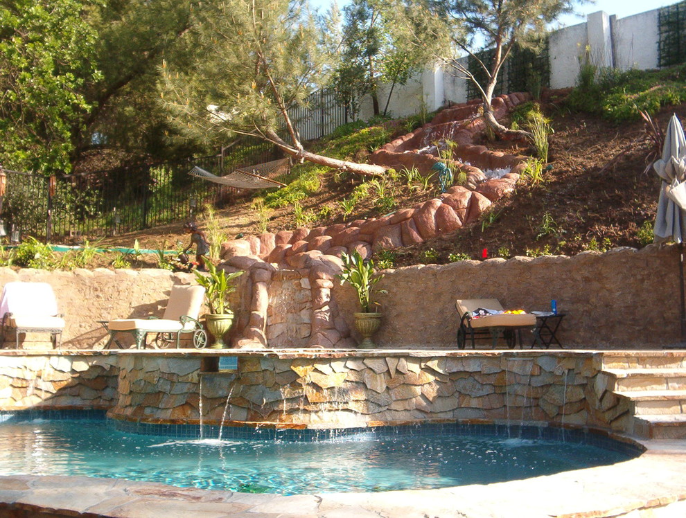 Immagine di una grande piscina naturale chic a "C" dietro casa con fontane e pavimentazioni in pietra naturale