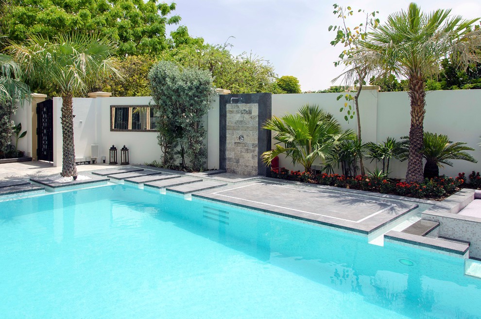 На фото: большой прямоугольный бассейн-инфинити на заднем дворе в современном стиле с фонтаном и покрытием из каменной брусчатки