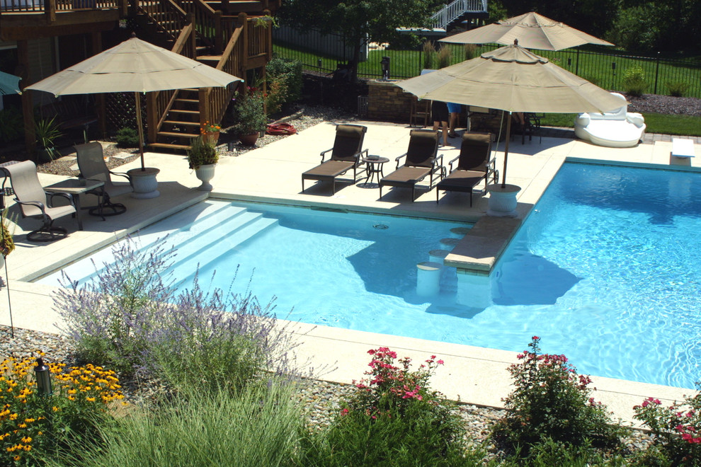 Ejemplo de piscina tradicional grande en forma de L en patio trasero con suelo de hormigón estampado
