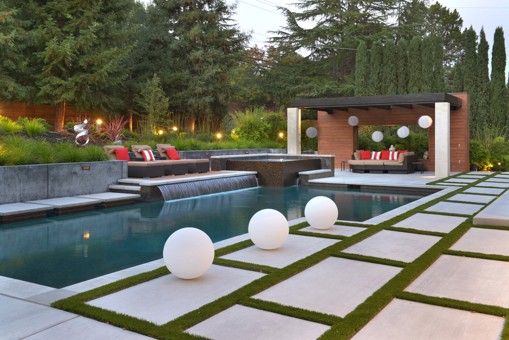 Immagine di un'ampia piscina design a "L" dietro casa con pavimentazioni in cemento e una vasca idromassaggio