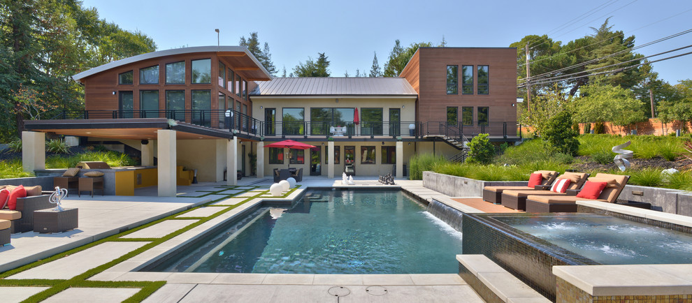 На фото: огромный бассейн произвольной формы на заднем дворе в современном стиле с джакузи и мощением тротуарной плиткой с