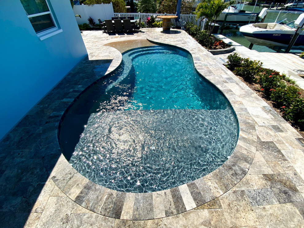 This is an example of a medium sized modern back custom shaped natural swimming pool in Tampa with a pool house and natural stone paving.
