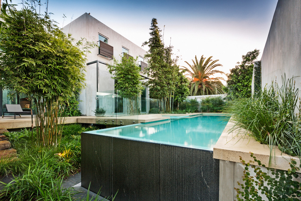 Modelo de piscinas y jacuzzis infinitos actuales de tamaño medio rectangulares en patio trasero con adoquines de hormigón