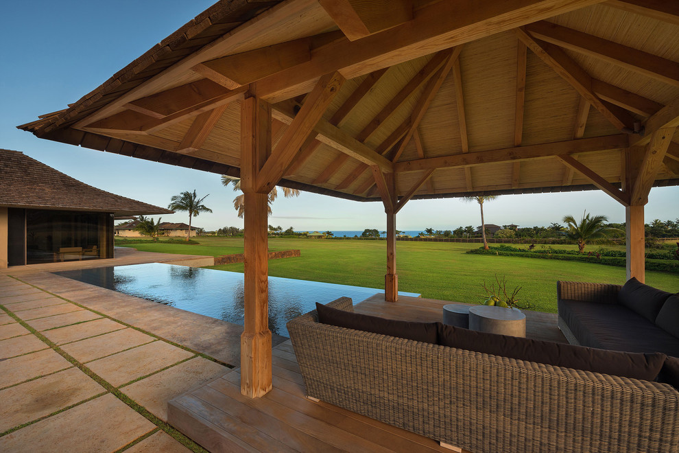 Diseño de piscina infinita tropical rectangular en patio trasero con adoquines de hormigón