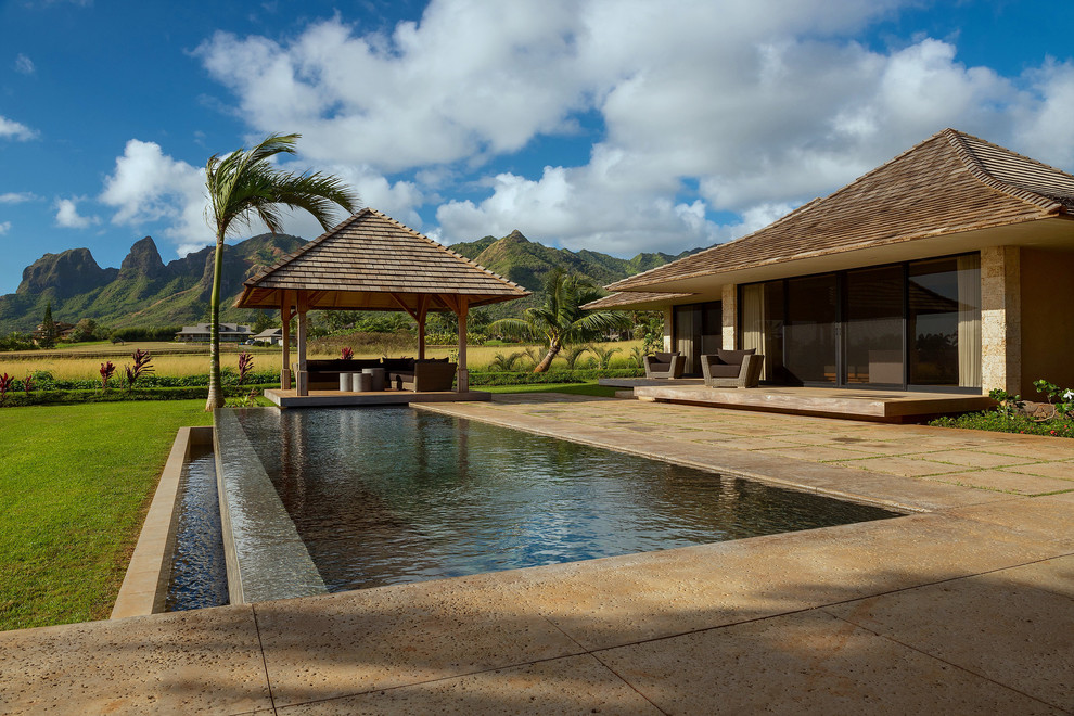 This is an example of a world-inspired back rectangular infinity swimming pool in Hawaii with concrete paving.