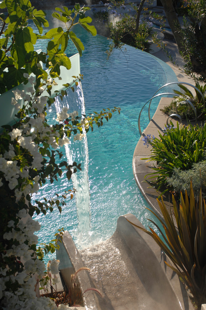 Diseño de piscina con tobogán infinita actual grande a medida en patio trasero con adoquines de piedra natural