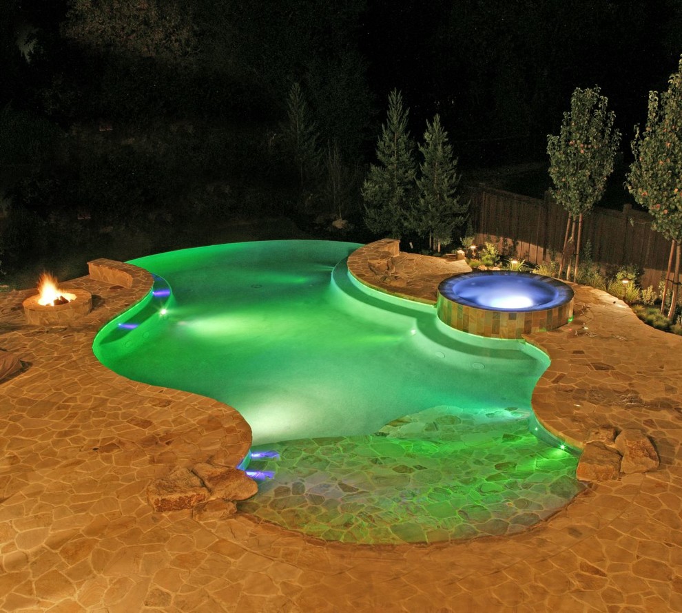 Cette image montre une très grande piscine à débordement et arrière traditionnelle sur mesure avec un bain bouillonnant et des pavés en pierre naturelle.
