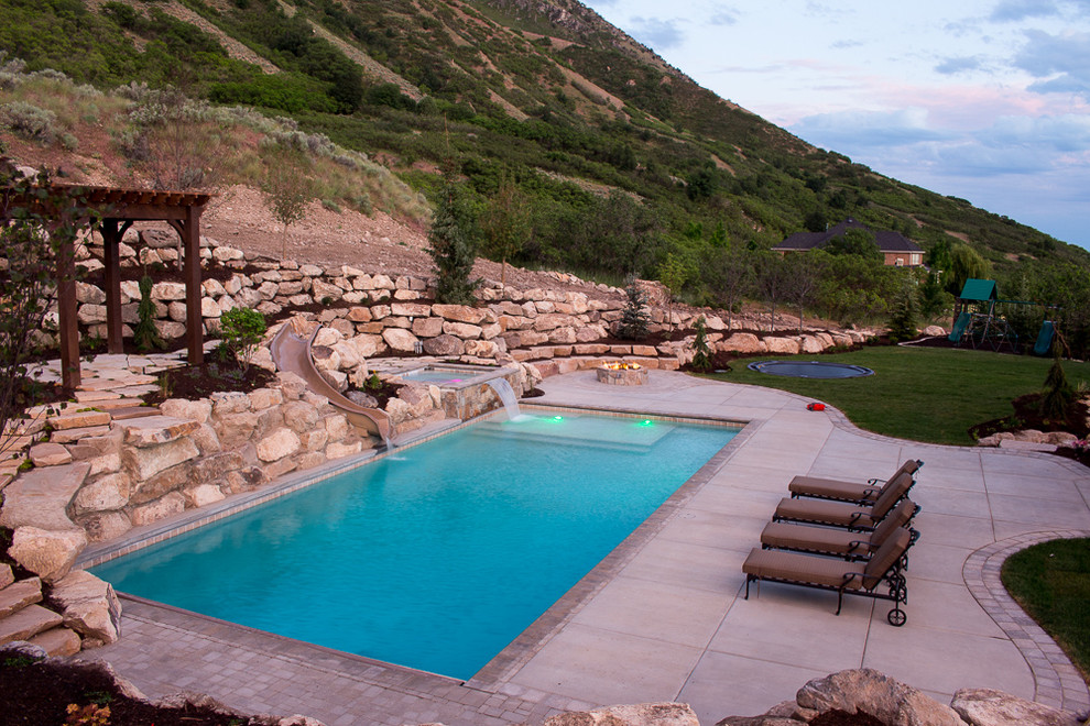 Foto de piscina con tobogán elevada de estilo americano de tamaño medio rectangular en patio trasero con adoquines de hormigón