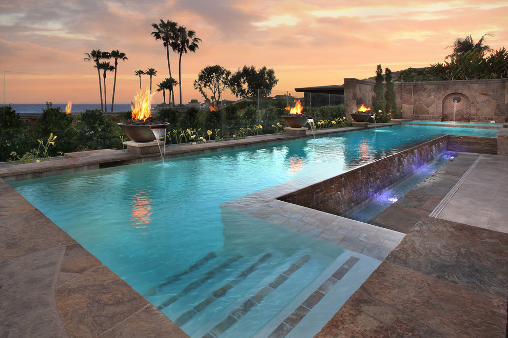 Imagen de piscina con fuente alargada mediterránea grande a medida en patio trasero con adoquines de piedra natural