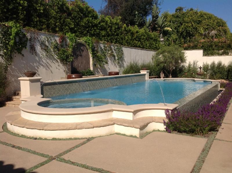 Foto de piscina con fuente infinita tradicional grande a medida en patio trasero con losas de hormigón