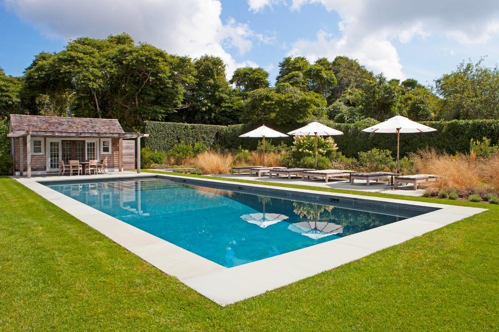 Large rural rectangular swimming pool in New York with a pool house and concrete paving.