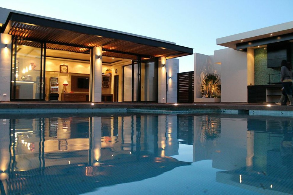 Modelo de casa de la piscina y piscina actual de tamaño medio rectangular en patio trasero con adoquines de piedra natural