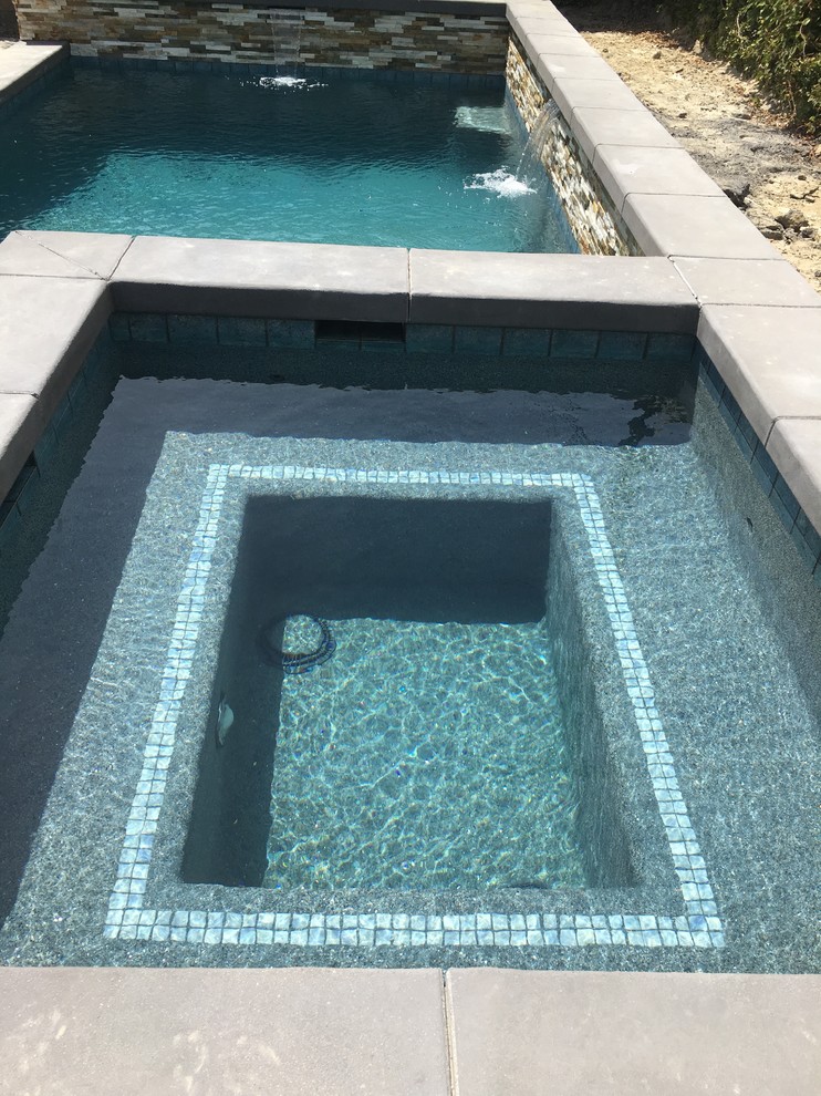 Ispirazione per una piscina monocorsia tropicale personalizzata di medie dimensioni e dietro casa con una vasca idromassaggio e lastre di cemento
