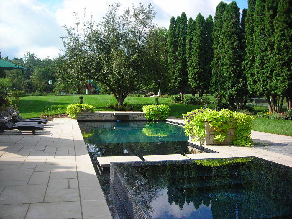 Inspiration for a large contemporary back custom shaped infinity hot tub in Grand Rapids with natural stone paving.