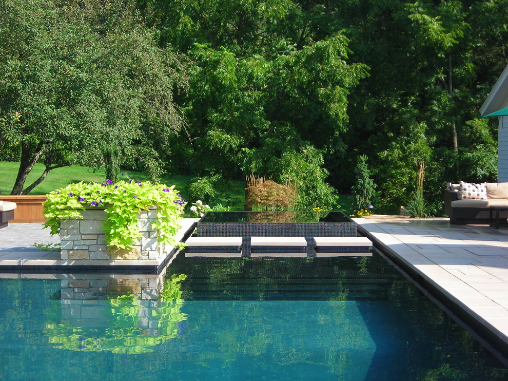 Réalisation d'une grande piscine arrière design sur mesure avec des pavés en pierre naturelle et un bain bouillonnant.
