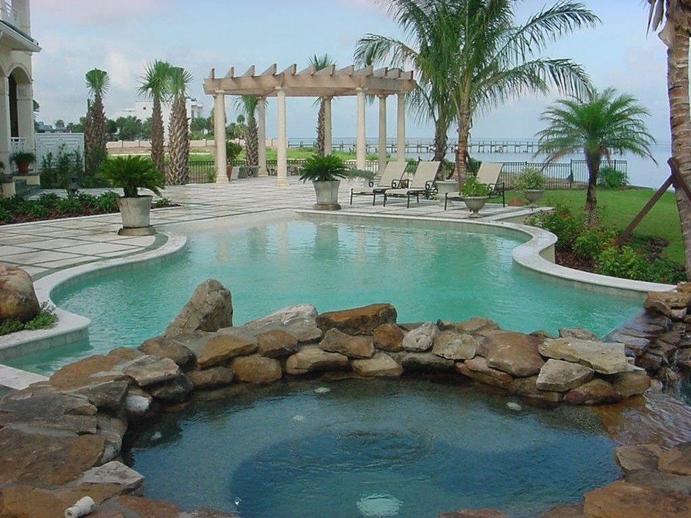 Bild på en stor tropisk anpassad pool på baksidan av huset, med spabad och marksten i betong