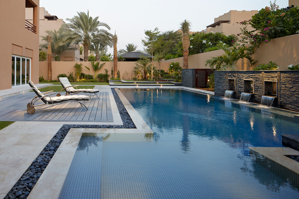 Diseño de piscina con fuente alargada mediterránea de tamaño medio en forma de L en patio trasero con suelo de baldosas