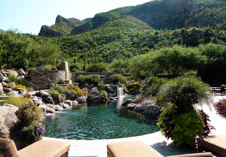 Exempel på en mycket stor modern anpassad pool, med en fontän och naturstensplattor